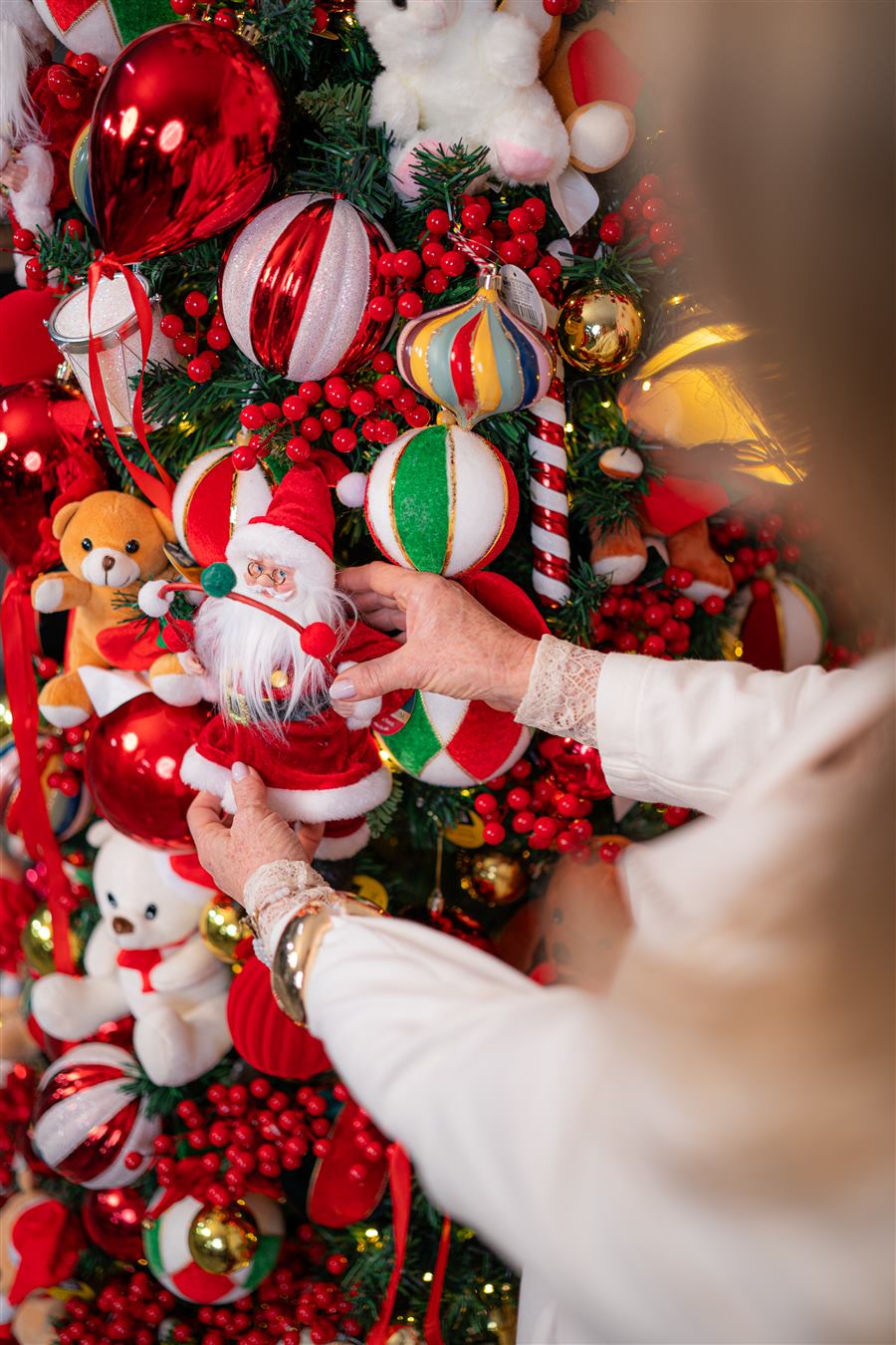 Rose, criadora da Rose Decor, sorrindo de braços abertos num cenário natalino estilo Circo Encantado, cercada de soldadinhos e Papais Noel.